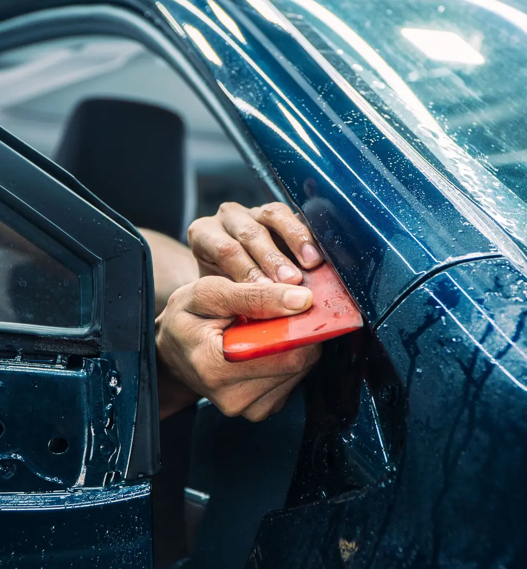 A hard card squeegee pressing window film flat at the edge of a car door